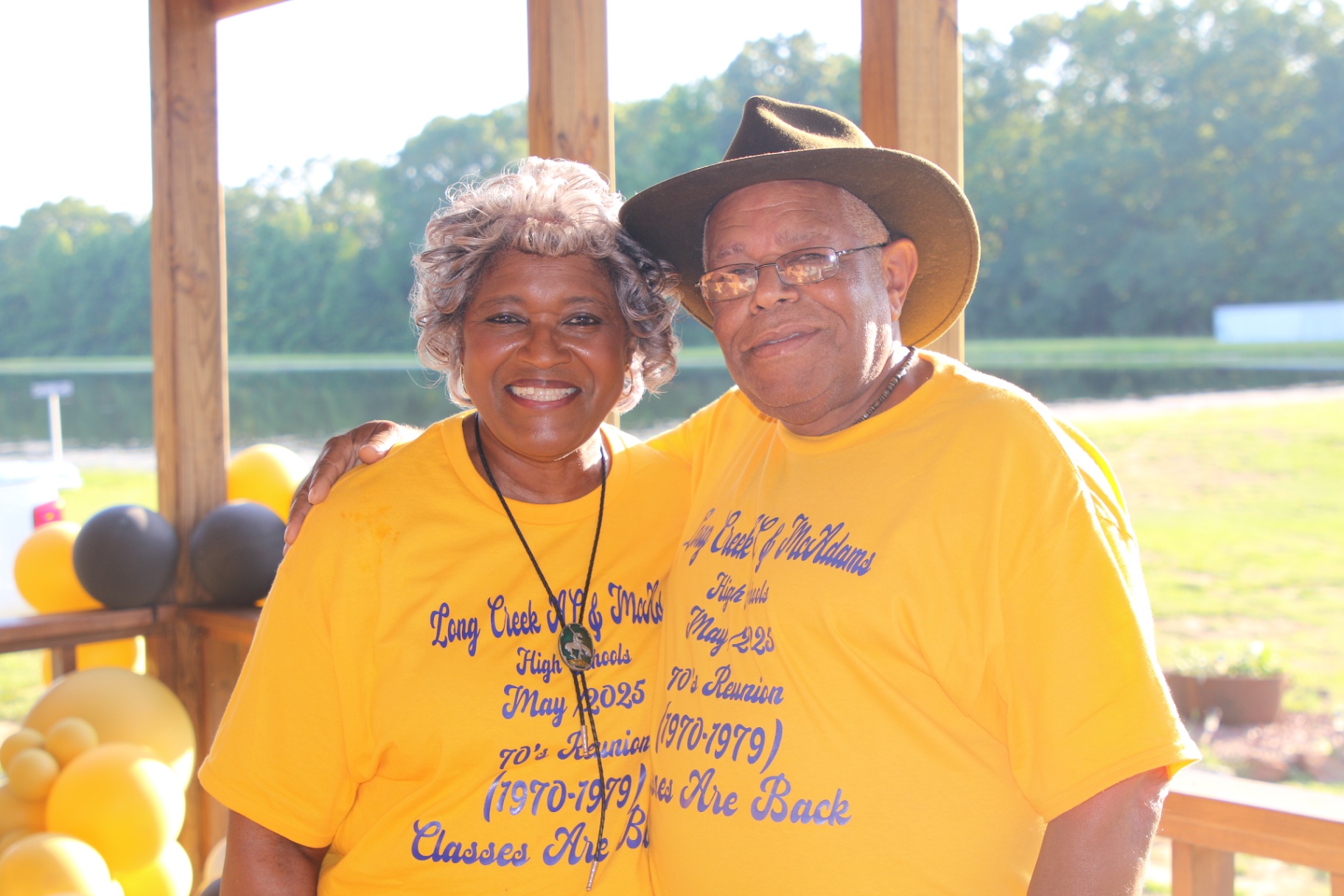 Couple in gold tees, cowboy hat, on the pavilion by the pond