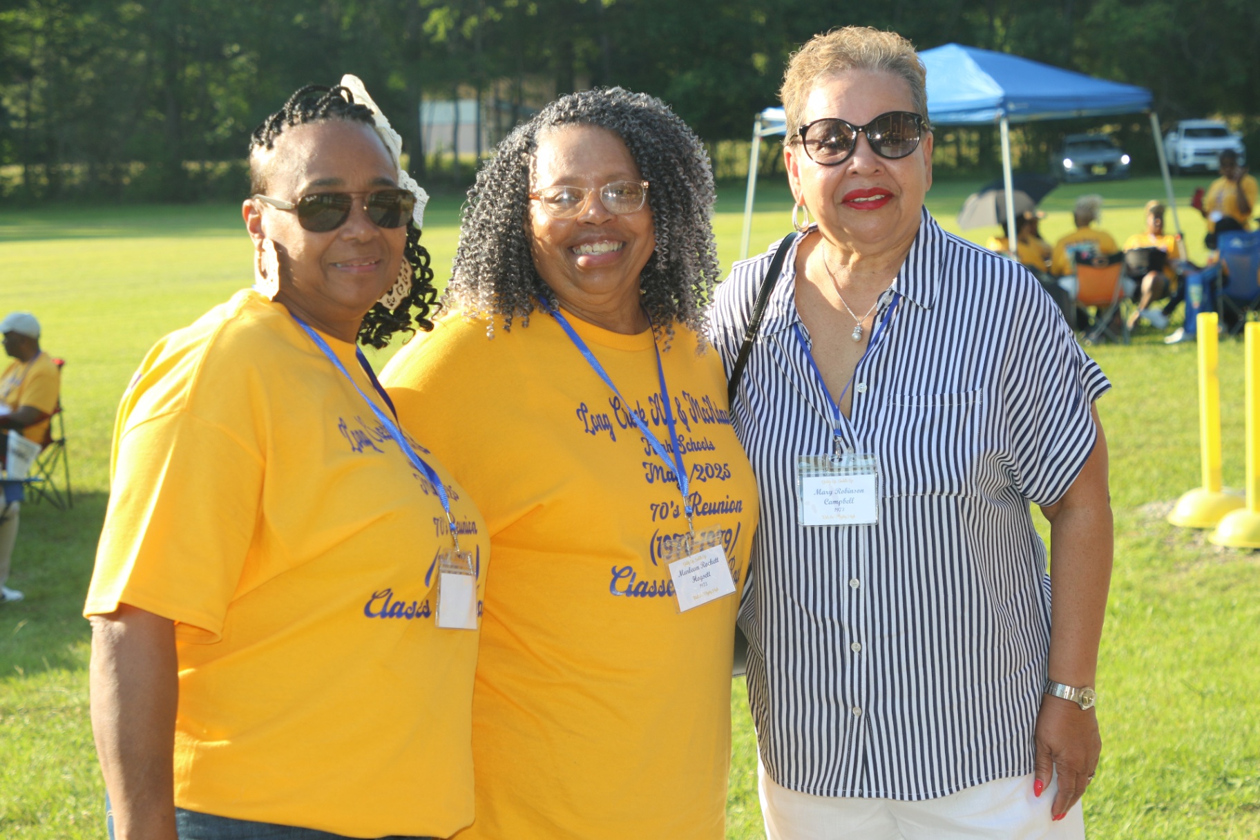 Three classmates smiling together in reunion gold